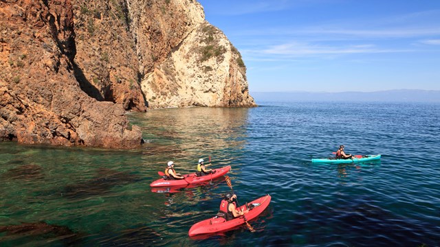 Red kayaks in blue water along coastal bluff. ©Tim Hauf, timhaufphotography.com